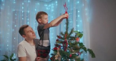 Babam Noel ağacının tepesine bir Noel yıldızı koymak için çocuğu kaldırdı. Baba ve oğul Noel ağacını birlikte süslerler.