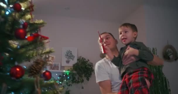 Baba çocuğu Noel ağacının tepesinde Noel yıldızı gibi giydirir. — Stok video