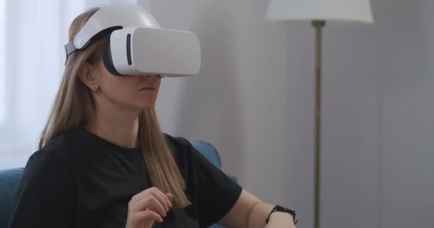 Usando la pantalla montada en la cabeza por una joven usuaria en casa, visualizando la pantalla y presionando botones virtuales, señora con auriculares VR — Vídeo de stock