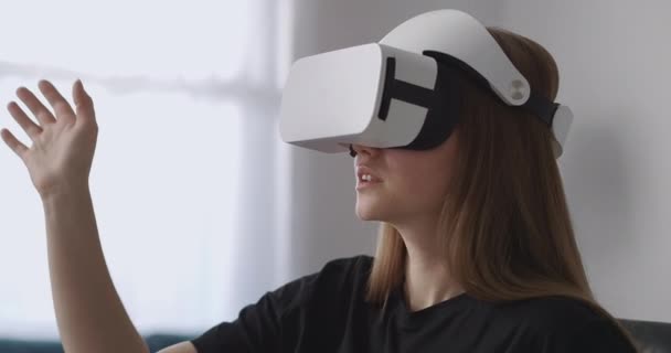 Γυναίκα χρήστης χρησιμοποιεί νέο κεφάλι-τοποθετημένη οθόνη για να παίζει παιχνίδια, κάθεται στο σαλόνι και κινείται τα χέρια για τον έλεγχο — Αρχείο Βίντεο