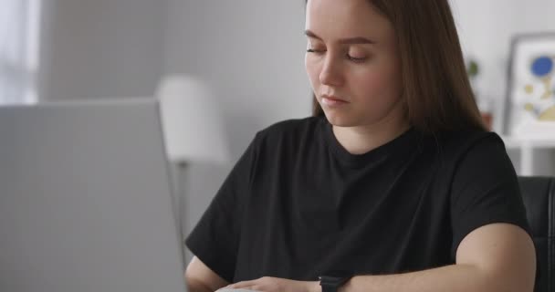インターネットによる自己教育、若い女性はノートパソコンを使いノートパソコンでノートを作る、リビングルームの女性の肖像画を作る、 — ストック動画
