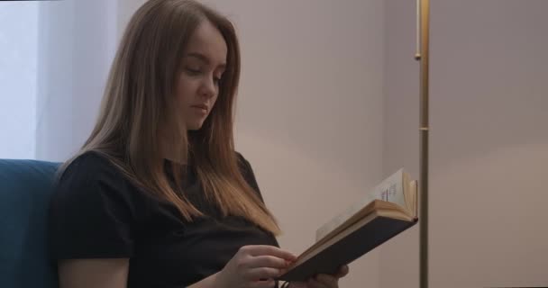 Jeune femme avec livre dans le salon le soir, fermeture et fermeture du lampadaire, portrait de femme à la maison le week-end, repos et auto-isolement — Video