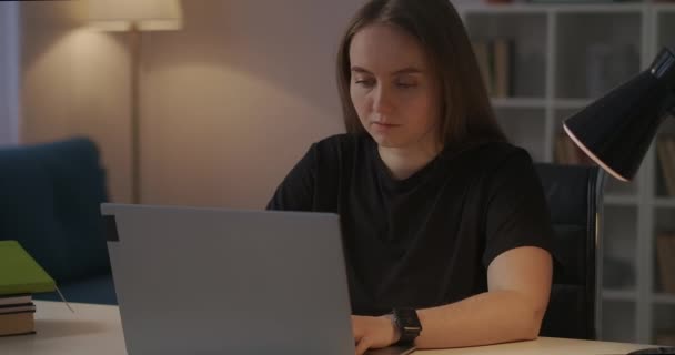 Estudiante femenina está trabajando con el ordenador portátil en casa por la noche, haciendo la tarea, estudiando en línea, preparándose para el seminario — Vídeo de stock