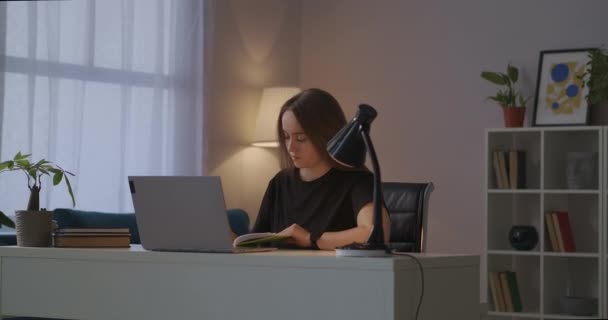 Woman is writing homework in notebook, reading information from screen of laptop, modern technology for education — Stock Video