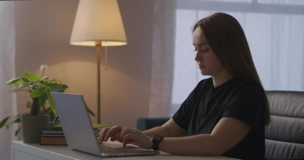 フリーランサーの女性は夜に自宅でノートパソコンを操作して首や骨粗しょう症や脊髄疾患の痛みを感じています — ストック動画