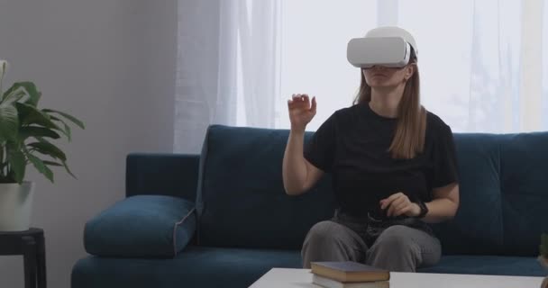 Giovane donna sta utilizzando moderno HMD-display sulla testa è seduto soggiorno, mani in movimento, il controllo da schermo virtuale — Video Stock