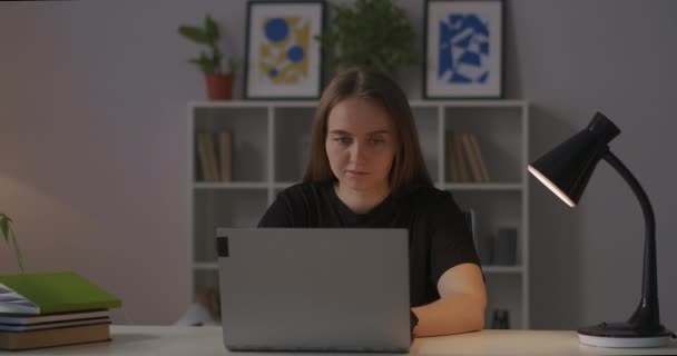 Young charming woman is using internet by laptop at evening, resting at home and surfing social media, sitting at table in living room — Stock Video