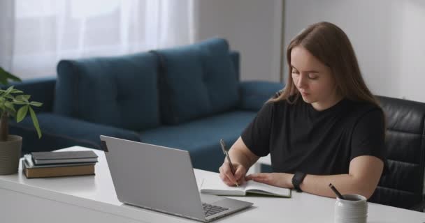 Fiatal diák nő hallgatja előadást videón laptop és írás jegyzetek notebook, távoli oktatás és e-learning, közepes portré — Stock videók