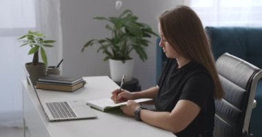 Kadın çevrimiçi ders izliyor, deftere notlar yazıyor, evden öğreniyor, uzaktan eğitim ve mesleki gelişim