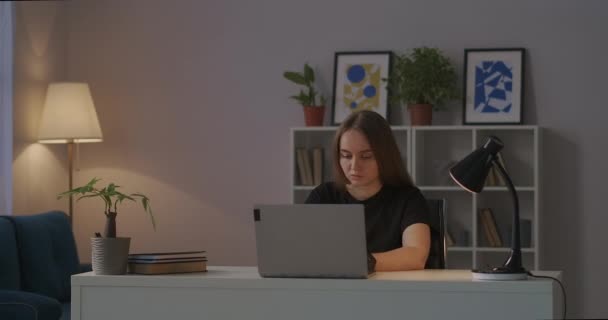 Mulher trabalhador remoto em seu escritório em casa à noite, sentado à mesa na sala de estar, trabalhando com laptop, conversando no chat de trabalho — Vídeo de Stock