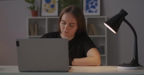 Γυναίκα σπουδάζει online, γράφει σημειώσεις στο σπίτι το βράδυ, κάθεται στο τραπέζι, πανοραμική λήψη γύρω της, μεσαίο πορτρέτο — Αρχείο Βίντεο