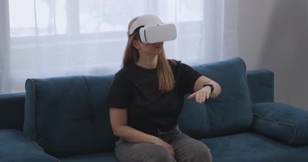 Donna con HMD-display sulla testa è seduto sul divano in appartamento, gesticolando per mano, realtà virtuale — Video Stock