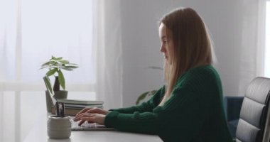 Serbest çalışan kadın dizüstü bilgisayarla mesaj yazıyor, evdeki masada oturuyor, evden internet işi yapıyor.