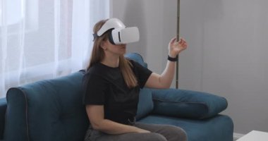Kadın kullanıcı modern dairenin içini görmek için HMD ekran kullanıyor, oturma odasında kanepede oturuyor, modern teknoloji