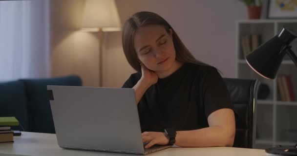 Κουρασμένη γυναίκα με πόνο στον αυχένα και οστεοχόνδρωση δακτυλογραφεί στο πληκτρολόγιο laptop, εργάζεται στο σπίτι το βράδυ, ασθένεια της σπονδυλικής στήλης και κούραση — Αρχείο Βίντεο