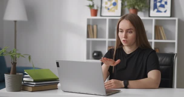 Woman is conducting webinar, sitting at home in front of laptop with web camera, talking and gesticulating, explaining and teaching — Stock Video