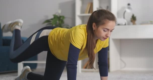 Atletische tiener meisje gekleed sportkleding is training thuis, spannen spieren van benen, fit te blijven, zorg over de gezondheid van het lichaam — Stockvideo
