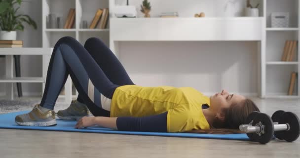 Jeune femme athlétique fait des exercices sportifs à la maison, soulevant les hanches pour l'entraînement des muscles, la forme physique et l'activité de bien-être — Video