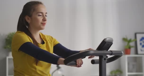 Calma giovane donna si allena con bicicletta fissa a casa, attività sportiva e stile di vita sano, ritratto medio — Video Stock