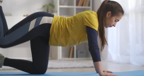 Jovem esbelta mulher está fazendo exercício esportivo para as pernas, treinando sozinho em casa, de pé no chão na sala de estar — Vídeo de Stock