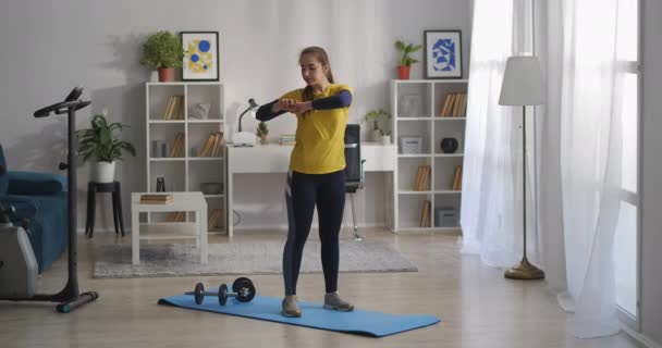 Девочка-подросток по утрам делает физические упражнения в гостиной современной квартиры, вытягивая руки — стоковое видео