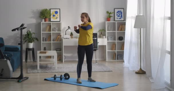 Ginástica para a coluna vertebral, mulher está treinando sozinho em casa no fim de semana, de pé sobre tapete desportivo e mãos móveis e tronco — Vídeo de Stock