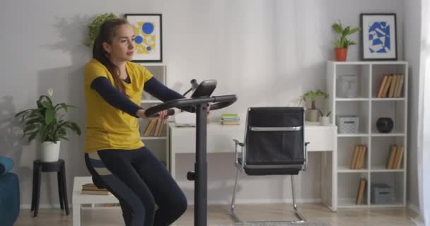 건강 한 생활 방식과 좋은 신체 조건, 젊은 여성은 혼자 집에서 훈련하고 있으며 자전거 페달을 돌리고 있다 — 비디오