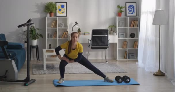 Aerobics och gymnastik träning hemma, tonåring flicka hukar på benen på sidorna, fitness i vardagsrummet — Stockvideo