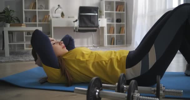 Mladá dáma je trénink břišní svaly, zvedání těla na kolena ležící na podlaze, cvičení doma, sportovní a zdravý životní styl — Stock video