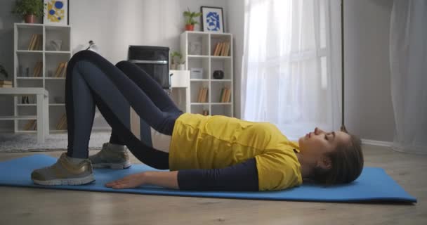 若い女性は足や腰の筋肉を訓練し家でのトレーニングフィットネスや健康的なライフスタイル床に横たわっ — ストック動画