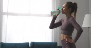 At kuyruklu güzel kadın antrenmandan sonra evde su içiyor. Jimnastikten sonra dinleniyor ve dinleniyor.