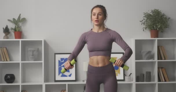 Mladá hezká žena dělá cvičení s činžáky v bytě, sportovní žena je školení v interiéru moderního bytu — Stock video