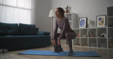 slender sportswoman is training ass and legs, crouching with weight in room of apartment, bodybuilding and fitness exercises at home
