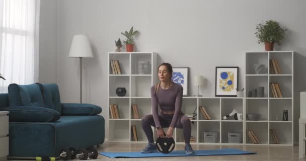 Squats avec poids, femme s'entraîne à la maison dans le salon, prise de vue complète dans l'intérieur moderne, mode de vie sain — Video