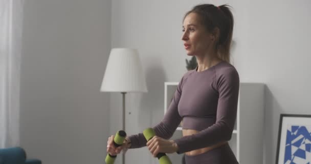 Sexy sporty woman with ponytail is training with dumbbells in flat, slender and muscular female body, keeping fit and losing weight — Stock Video