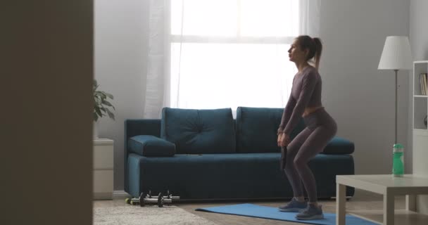 Sexy dame met paardenstaart doet hurken met gewicht in handen, training billen en benen spieren, home fitness oefeningen — Stockvideo