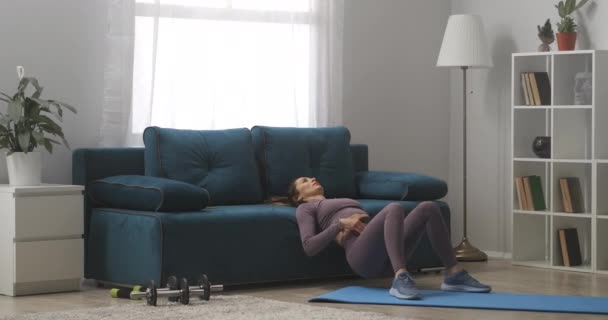 Casalinga sta facendo esercizi per i muscoli addominali a casa, appoggiato sul divano in soggiorno, sollevamento fianchi — Video Stock