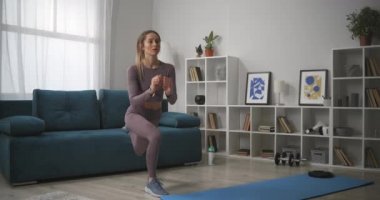 Güzel genç bir kadın oturma odasında çömeliyor. Spor ve sağlıklı bir yaşam tarzı. Salgın hastalıkta kendini izole ediyor.