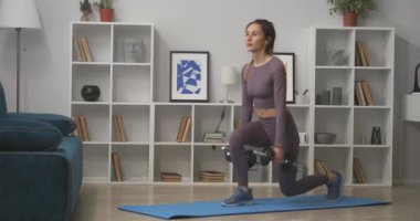 Elinde dambıllarla çömelmiş, hafta sonları evde antrenman yapan, formda ve kilo veren bir kadın.