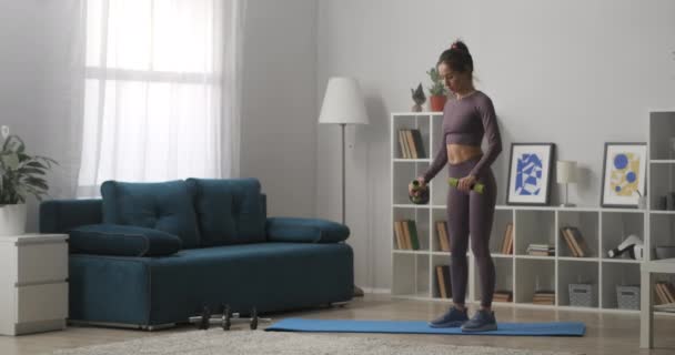 Gym bunny vrouw is training thuis met halters, houden van goede vorm, slanke dame gekleed sportieve kleding, gezonde lifstijl — Stockvideo