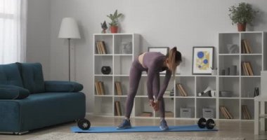 At kuyruklu güzel bir kadın sabah antrenmanı sırasında eğiliyor. İnce yapılı, modaya uygun, sıska spor giyinen, evdeki sporcu kadın.