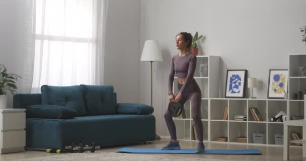 Фитнес дома, молодая женщина приседает с весом в гостиной, спортивный и здоровый образ жизни, поддерживая себя в форме во время самоизоляции — стоковое видео