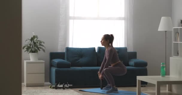 Femme sportive habillée vêtements de sport fait squats avec du poids dans les mains, corps d'entraînement, garder la forme, plan complet dans l'appartement — Video