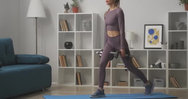 Athletic woman is squatting with dumbbells in hands at home, keeping fit and losing weight, working muscles of ass — Wideo stockowe