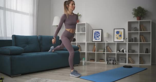 여자는 거실에서 다리 근육 운동을 하고, 운동을 하고, 운동을 하고, 가정 훈련과 건강을 위해 운동을 하고 있다 — 비디오