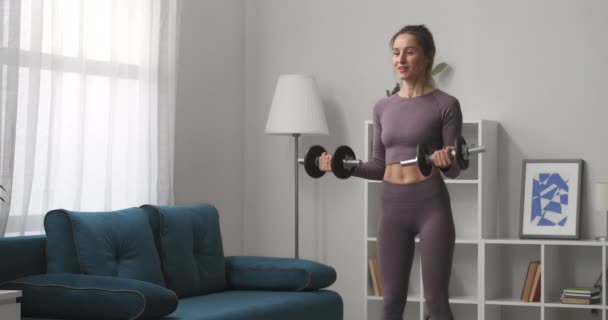 Esportista ativo está levantando halteres, treinamento em casa sozinho e sorrindo, retrato de senhora atlética no apartamento, estilo de vida saudável — Vídeo de Stock