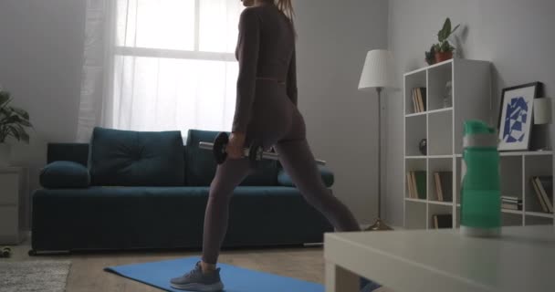 Idrottskvinna tränar ensam hemma, hukar sig med hantlar i händerna, arbetar muskler ben och skinkor, träning på helgen — Stockvideo