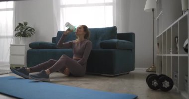 Sakin ol, spor tavşanı hafta sonları evde antrenman yaptıktan sonra yerde oturup su içiyor ve dinleniyor.