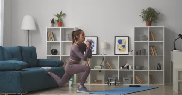 Mujer joven con cola de caballo está haciendo sentadillas en casa, entrenamiento solo en la sala de estar en fin de semana, estilo de vida saludable y deportivo — Vídeo de stock