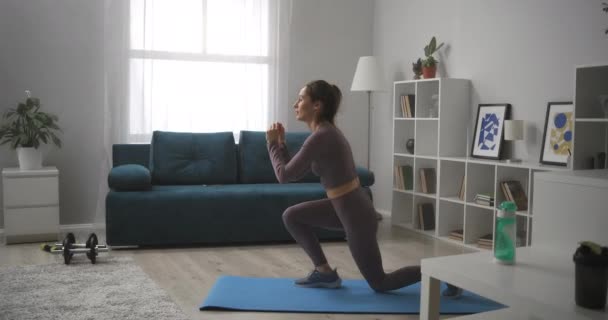 Mujer deportiva y activa está entrenando en casa, saltando y en cuclillas, aptitud en cuarentena y encierro — Vídeo de stock